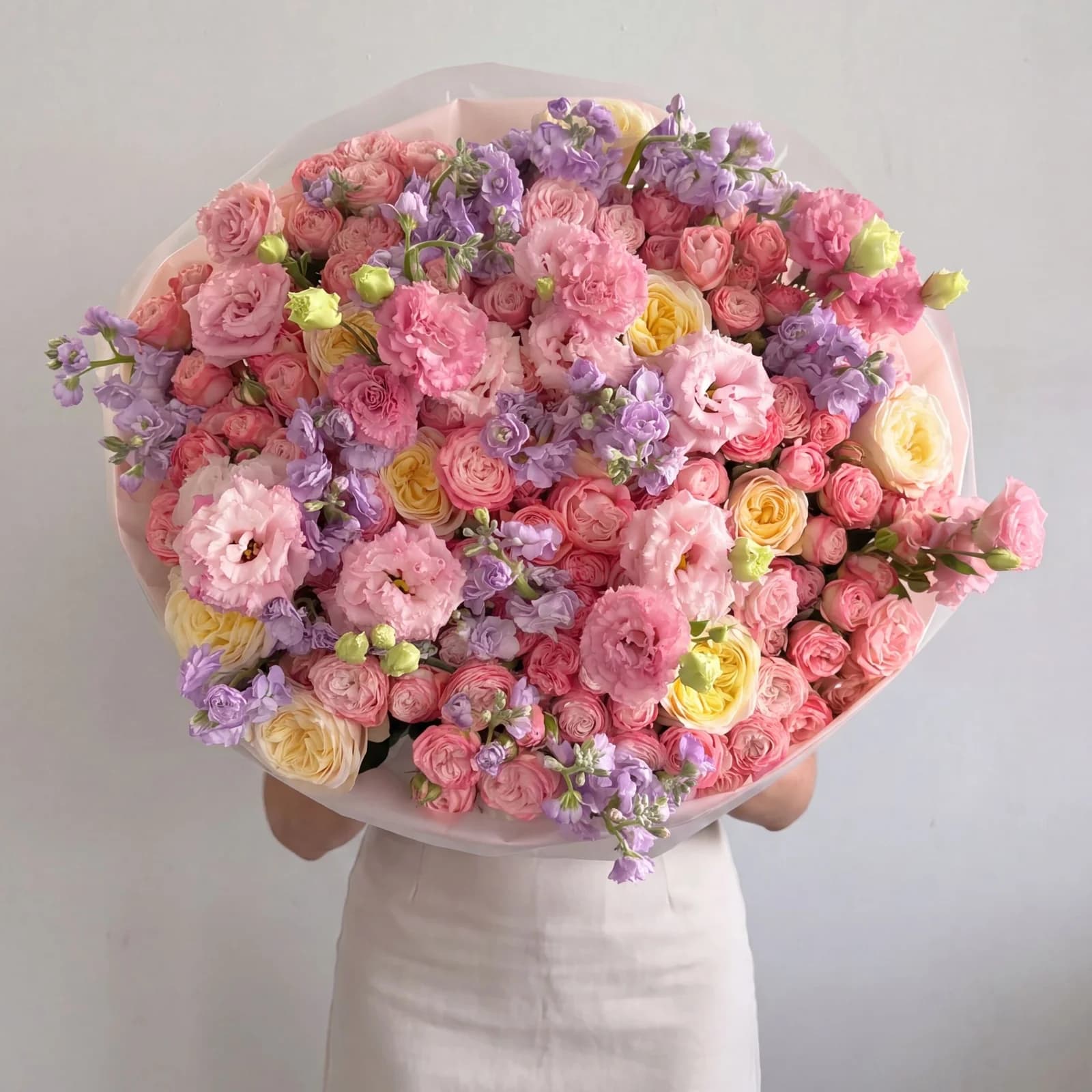 An armful of pastel flowers, with pink spray roses, lisianthus, lilac stock and cream garden roses in blush wrap