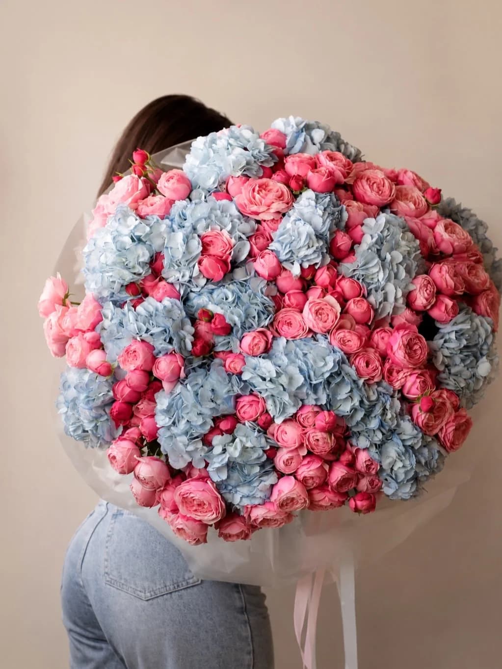 A woman carrying an oversized bouquet of pink spray roses and pale blue hydrangeas over her shoulder