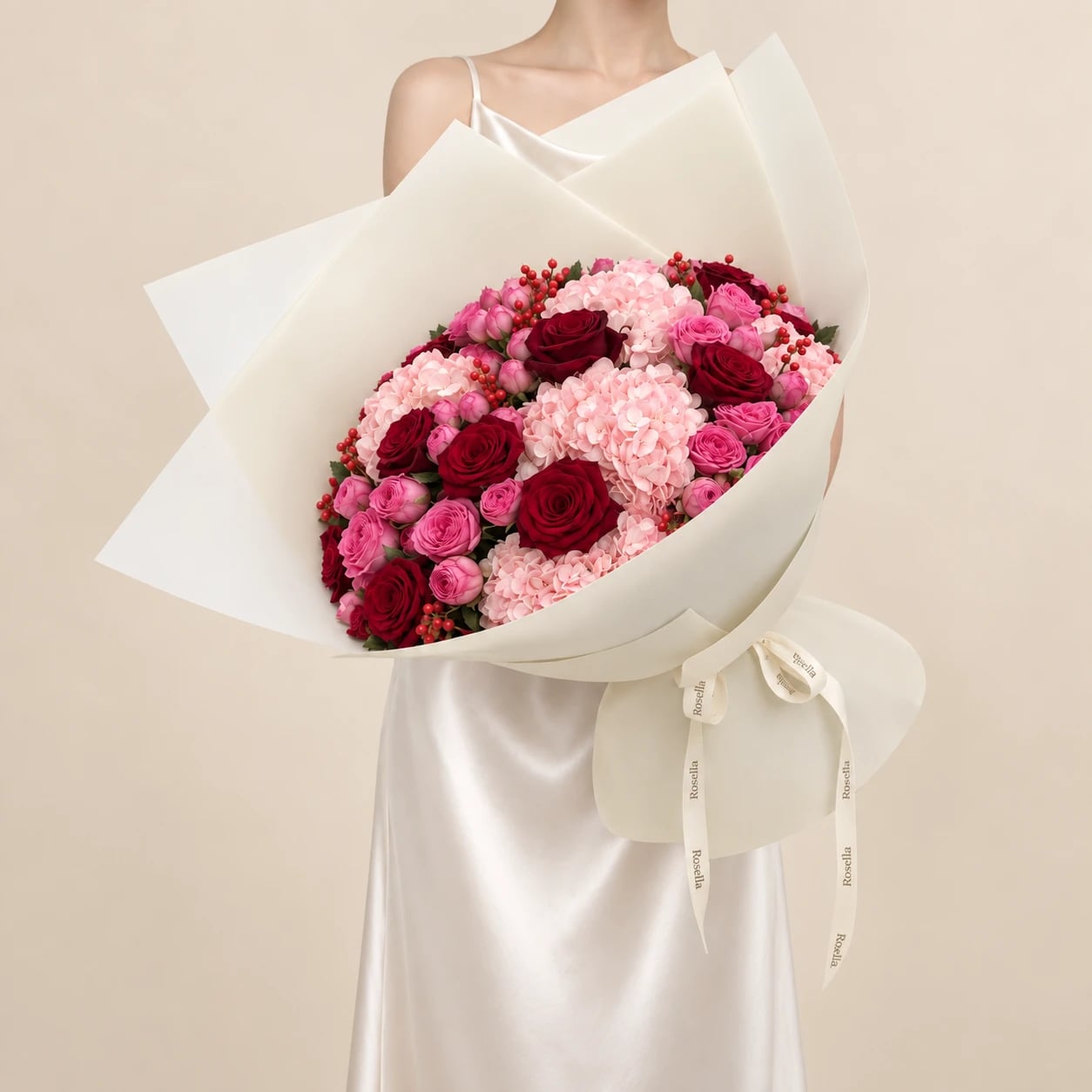 A generous bouquet of red roses, pink spray roses, blush hydrangeas and red berries, wrapped in ivory paper and tied with a Rosella ribbon